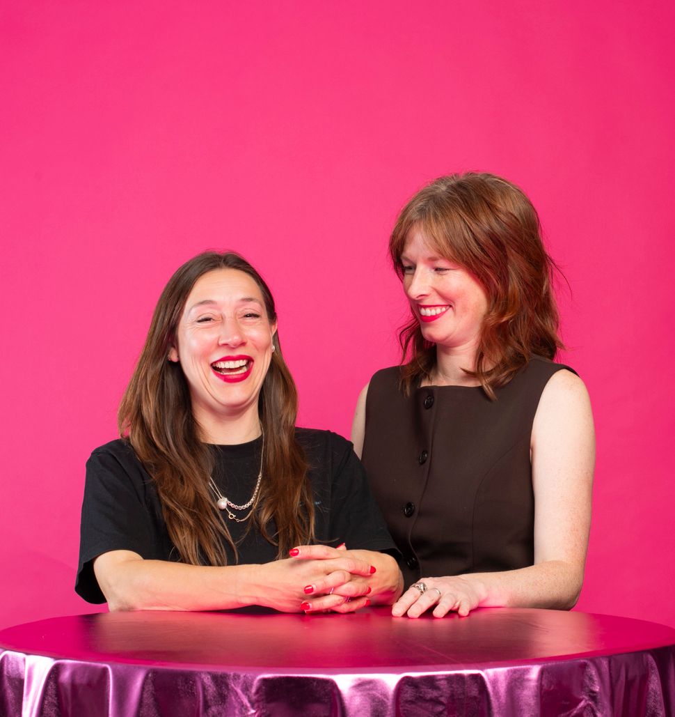 Twee lachende vrouwen aan een tafel, in monochroom blauw
